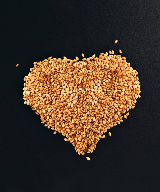 toasted white sesame seeds arranged in a shape of heart on a smooth black table surface